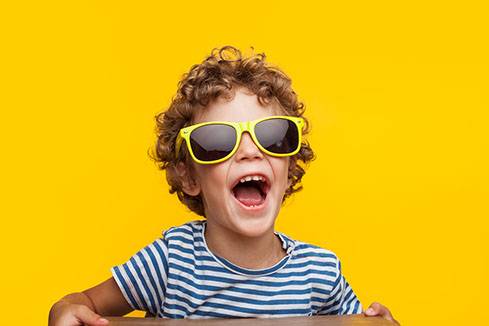 Portrait of cheerful little boy wearing adult sunglasses and looking away on orange background.